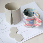 Ceramic mug template with abstract design on a white surface with clay pieces and templates.