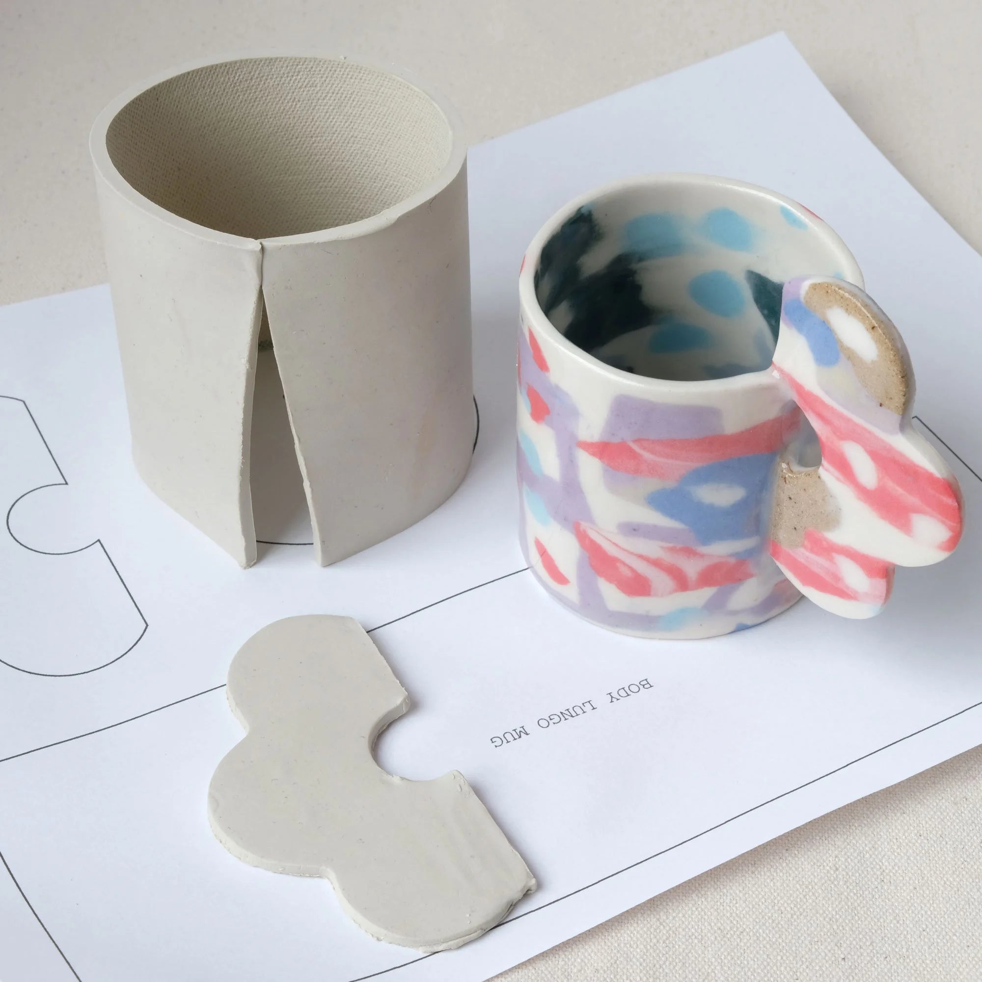 Ceramic mug template with abstract design on a white surface with clay pieces and templates.