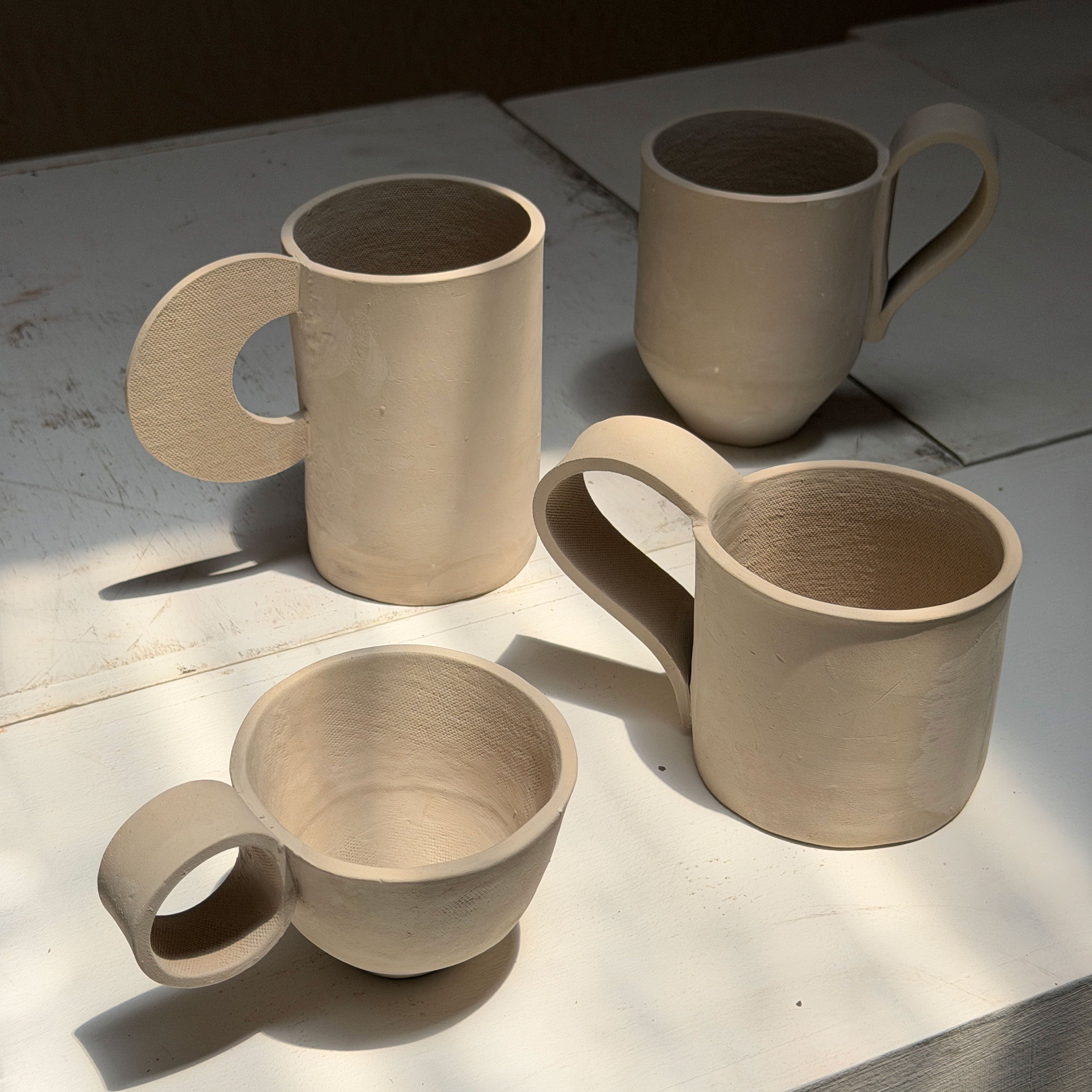 Four ceramic slab template mugs on a light surface with a dark background