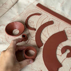 Hand holding a terracotta pot piece on a surface with clay pottery patterns