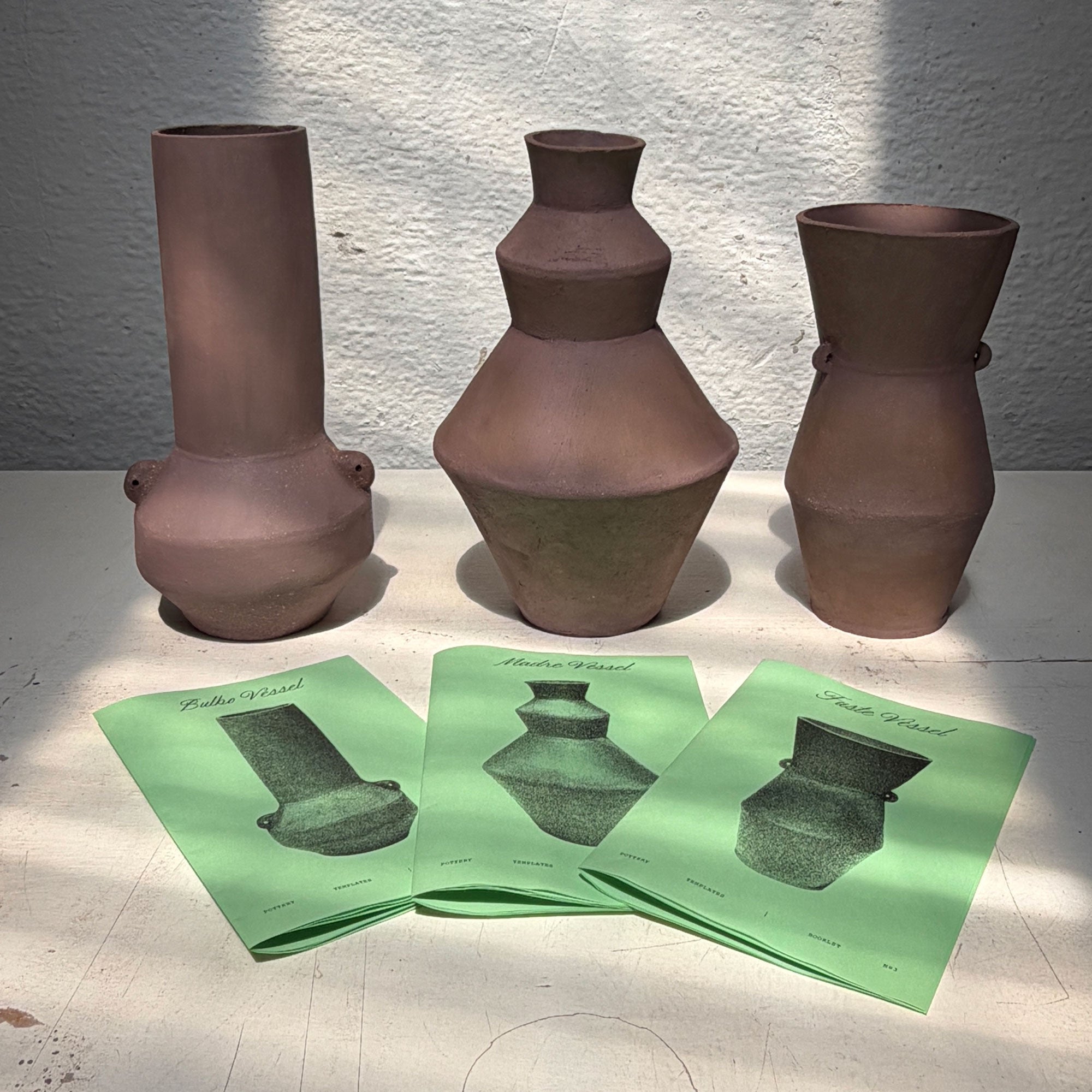 Pottery bundle ceramic vases on a light surface with three green brochures featuring images of the vases.